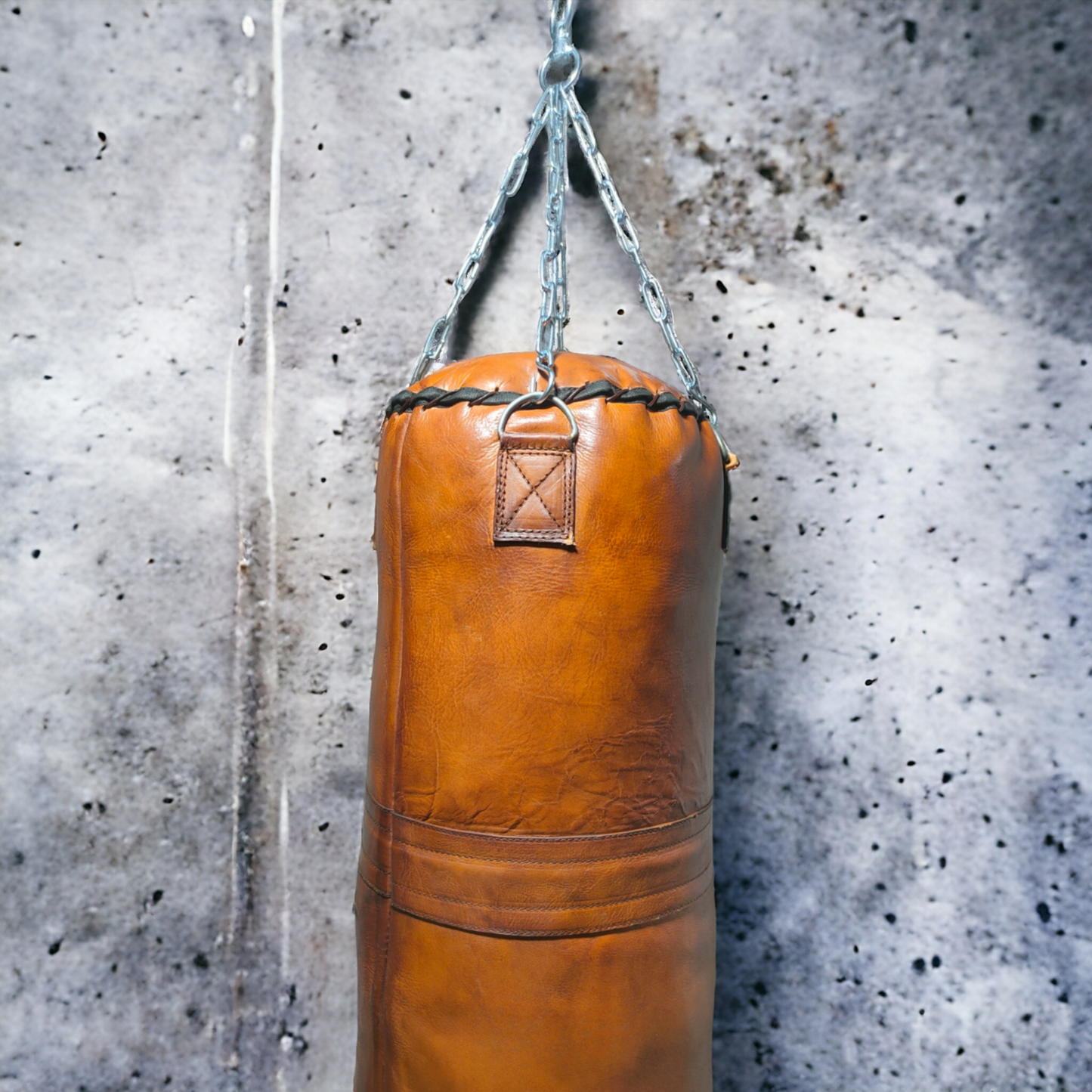 leather punching bag made from vegetable tan hANGING FROM THE CEILING agaisnt rey wall