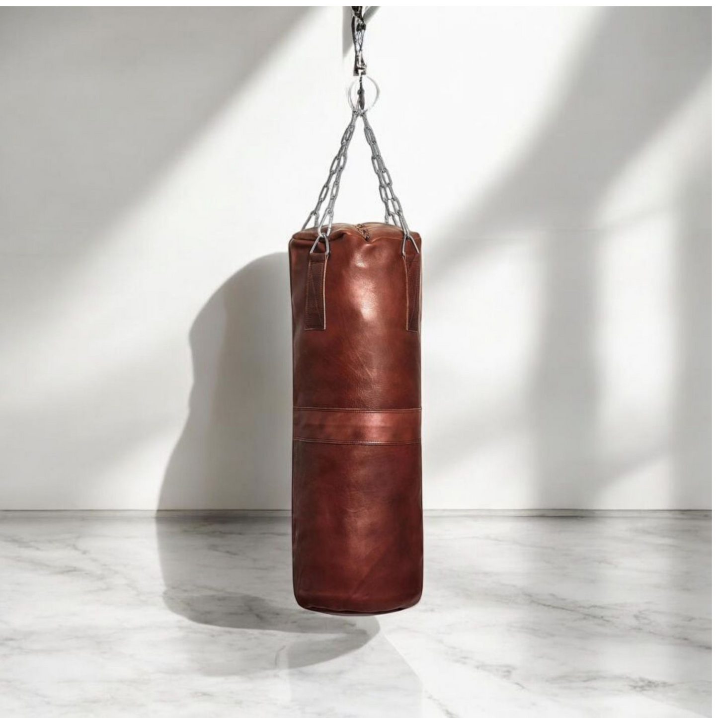 A large Blood-Fang Pro Punching Bag (up to 6 feet) hanging by its professional steel chain for a full-body MMA Kickboxing Bag or Boxing Training Equipment session. The heavy-duty cowhide genuine leather heavy bag is shipped as an unfilled punching bag, allowing customization. This handmade heavy bag is essential Gym Workout Gear and a classic vintage leather punching bag for any combat sport/ leather punching bag, heavy bag, boxing bag, kickboxing bag, Muay Thai heavy bag, free standing punching bag