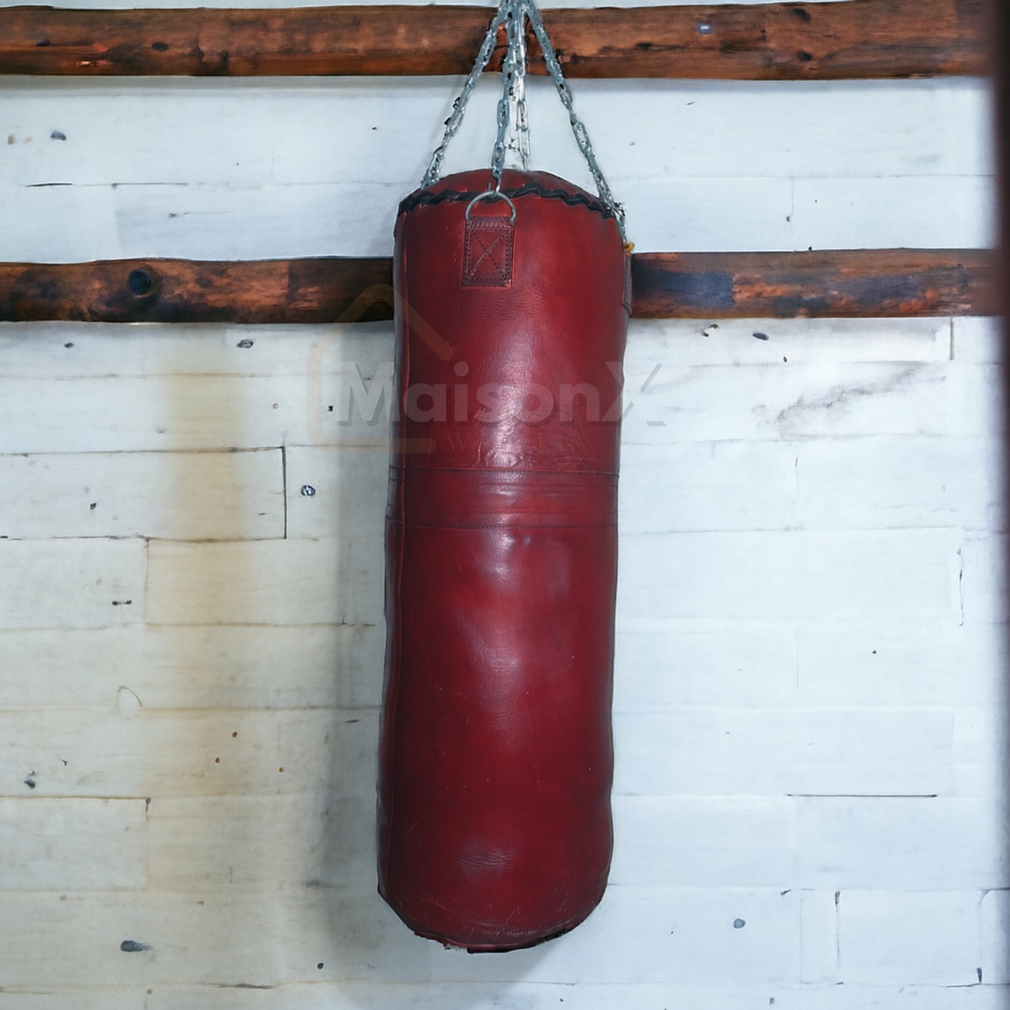 burgundy leather heavy bag for training hung against vintage wall with stainless steel chain of silver color. wall have 2 wood logs