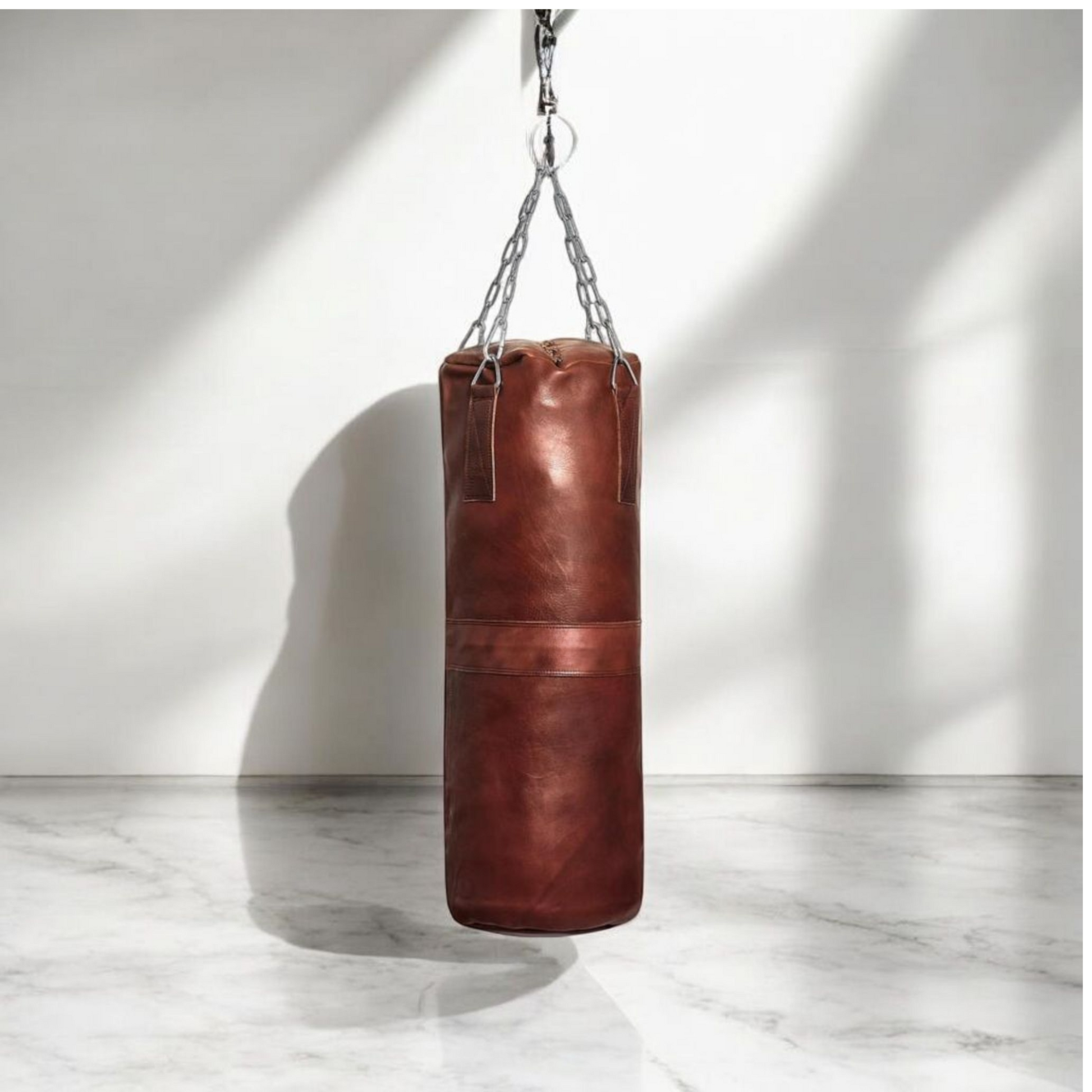 A large Blood-Fang Pro Punching Bag (up to 6 feet) hanging by its professional steel chain for a full-body MMA Kickboxing Bag or Boxing Training Equipment session. The heavy-duty cowhide genuine leather heavy bag is shipped as an unfilled punching bag, allowing customization. This handmade heavy bag is essential Gym Workout Gear and a classic vintage leather punching bag for any combat sport/ leather punching bag, heavy bag, boxing bag, kickboxing bag, Muay Thai heavy bag, free standing punching bag