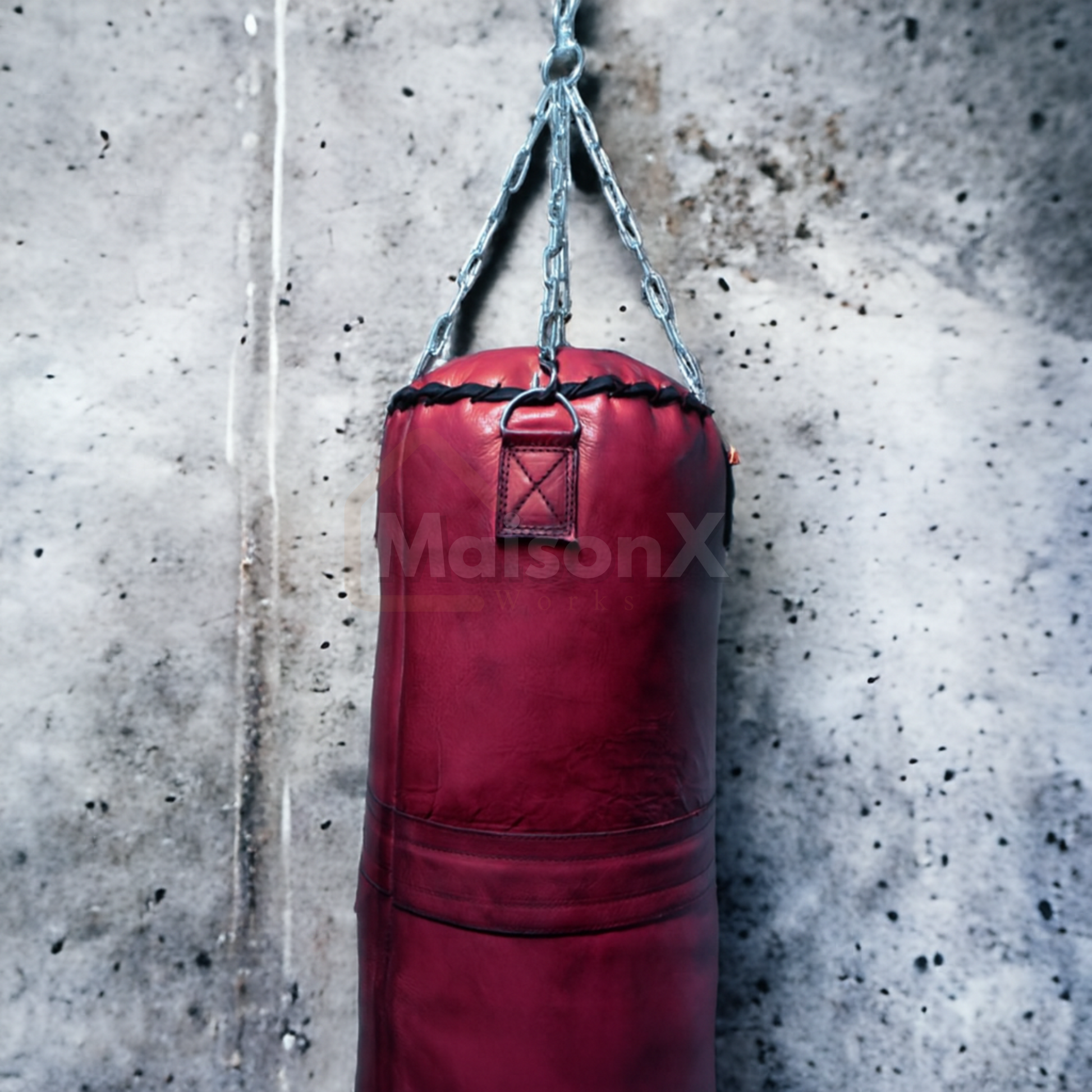 leather heavy punching bag made of cowhide leather maroon color with stainless steel chain hung against concrete wall.