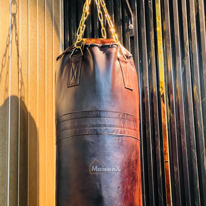vintage leather heavy punching bag hung with golden chains infront of black and gold background. Cowhide leather used for heavy duty training for boxing and mma practice. High quality image of punching bag for home gyms, commercial gyms.