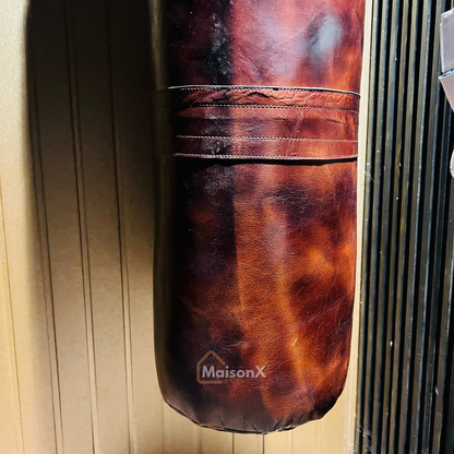 vintage leather heavy punching bag hung with golden chains infront of black and gold background. Cowhide leather used for heavy duty training for boxing and mma practice. High quality image of punching bag for home gyms, commercial gyms. one of a kind leather punching bag. brown burgundy coloe leather heavy bag for heavy duty training that stands the test f time. punching bag hanging with golden chains infront of gold and black wall. closeup image of leather punching bag from below