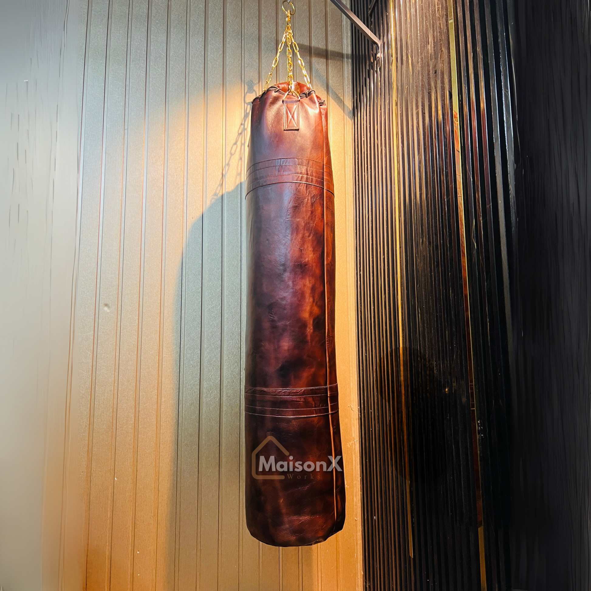 vintage leather heavy punching bag hung with golden chains infront of black and gold background. Cowhide leather used for heavy duty training for boxing and mma practice. High quality image of punching bag for home gyms, commercial gyms. brown burgundy color leather punching bag complete picture. best punching bag ever. unique and luxurious punching bag that actually last long. original leather