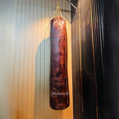 vintage leather heavy punching bag hung with golden chains infront of black and gold background. Cowhide leather used for heavy duty training for boxing and mma practice. High quality image of punching bag for home gyms, commercial gyms. brown burgundy color leather punching bag complete picture. best punching bag ever. unique and luxurious punching bag that actually last long. original leather