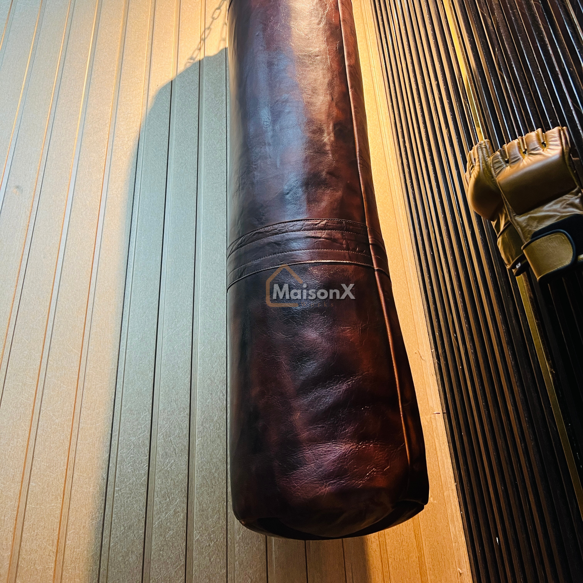 picture of leather punching bag of burgundy color from below showing the downward portion of the leather punching bag, with mma gloves hanging by side. a classy product for combat sports, perfect gift for people into mma training, fitness and home gym, christmas gift